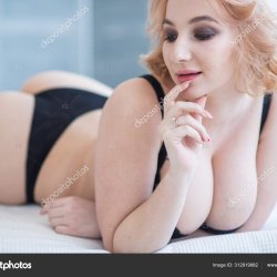 A European girl with a cute face and big Breasts in black underwear lies on her stomach. Very sexy. Stock Photo inside-studio 312919982